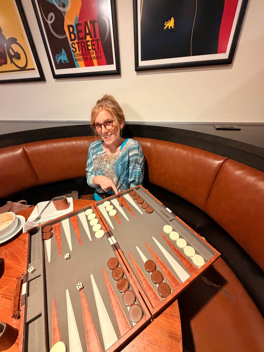 Tabitha Lovell pointing at the backgammon board from a leather booth