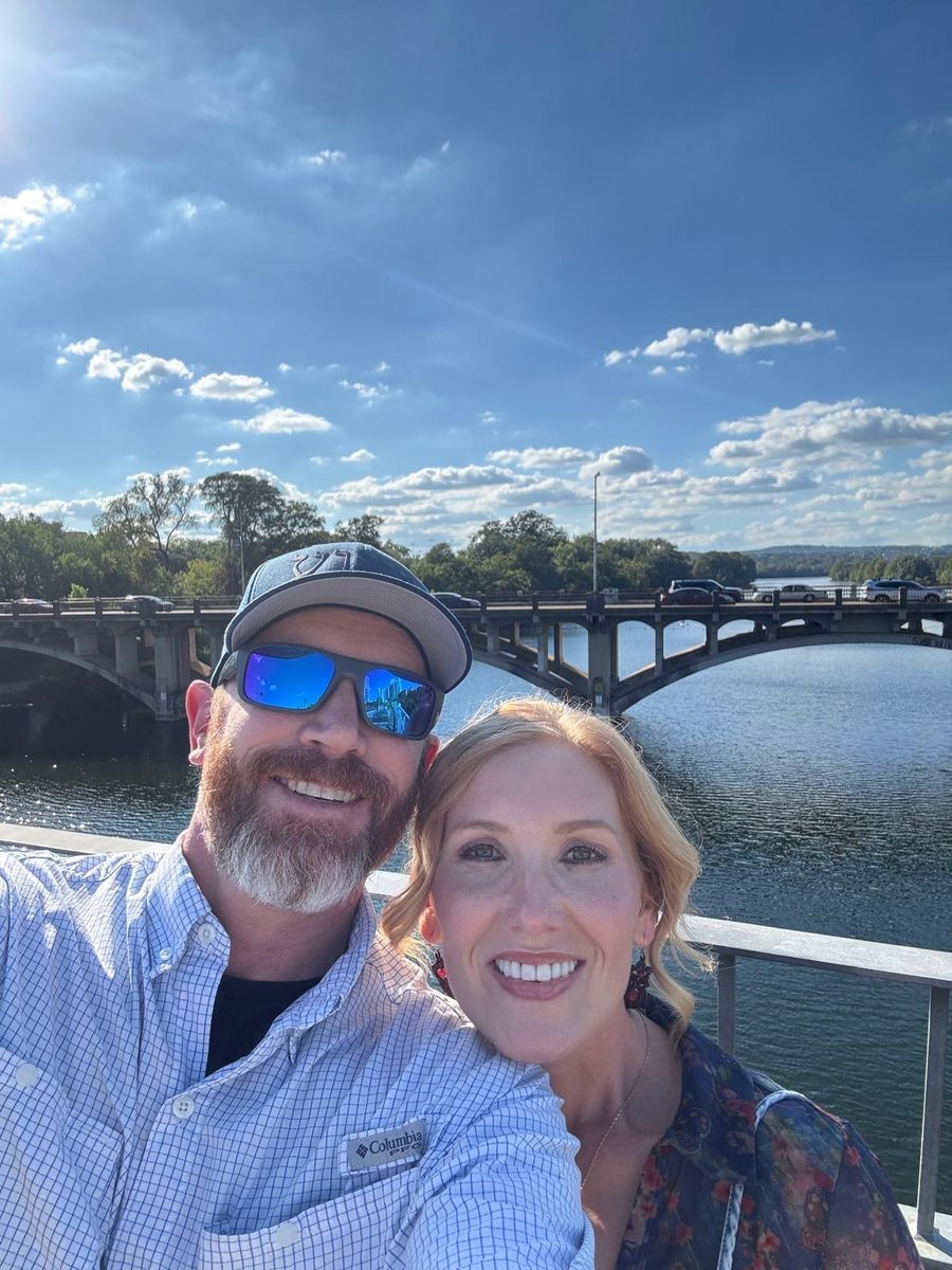 Tabitha and Kevin Lovell on a bridge over Lady Bird Lake in Austin under a big blue sky